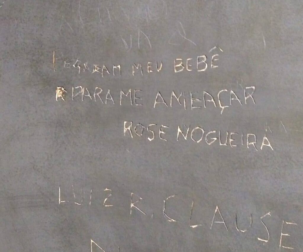 Fotografia de uma parede em que foi escrito "pegaram meu bebê para me ameaçar. Rose nogueira", em vermelho acima esta escrito " fora ditadura asssassina", abaixo tem alguns nomes escritos como " Luiz R. Clause" e Diva Burn"